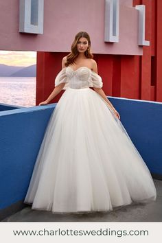 a woman in a white wedding dress standing on a wall next to the ocean with her hands on her hips