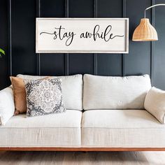 a white couch sitting under a wooden sign that says stay awhile on the wall above it