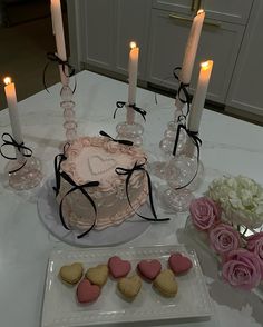 a table topped with a heart shaped cake next to two candles and some cookies on top of a plate