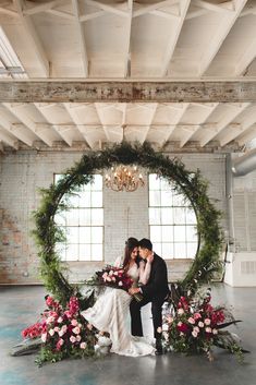 a bride and groom sitting in front of a floral wreath