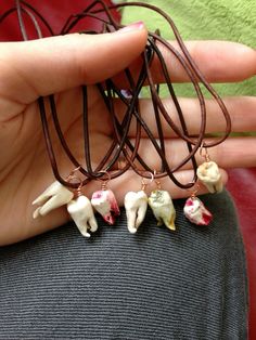 a person holding four small tooth necklaces in their hands, one is white and the other is brown