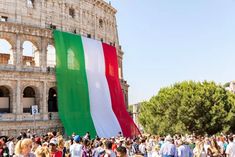 people walking around in front of an old building with a large italian flag hanging from it's side