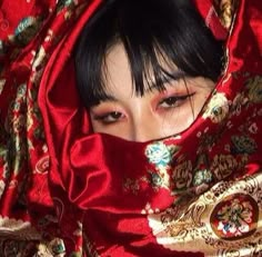 a woman with black hair wearing a red shawl over her head and looking at the camera