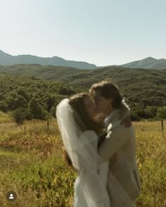 a bride and groom kissing in a field with mountains in the background on their wedding day