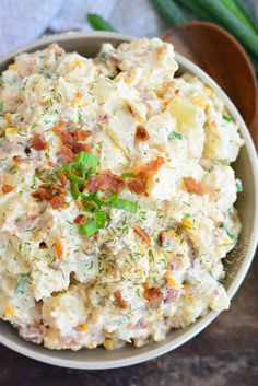 a bowl filled with potato salad on top of a wooden table next to green onions