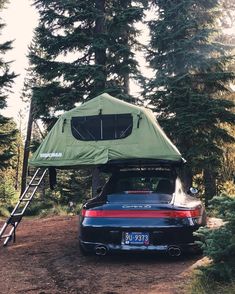 a car parked in the woods with a tent on it's roof and ladder