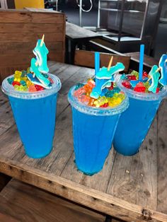 three blue drinks with candy in them sitting on a wooden table next to each other