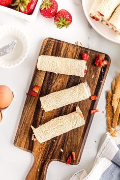 sliced sandwiches on a cutting board next to eggs and strawberries