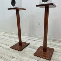 two speakers on wooden stands in front of a white wall