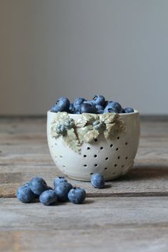 a white bowl filled with blueberries sitting on top of a wooden table next to some berries