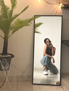 a woman taking a selfie in front of a large mirror with a plant behind her