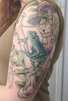 a woman with a frog tattoo on her arm and shoulder, holding onto a tree branch