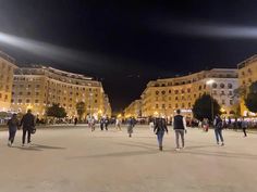 people are walking around in the middle of a city square at night with lights on