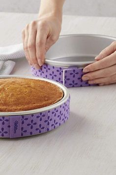 a person is placing a cake in a pan on the table with a purple ribbon around it