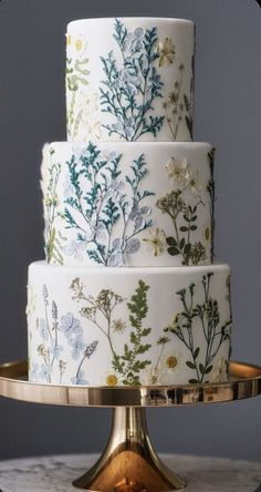 a three tiered cake decorated with flowers and leaves on a gold plated stand