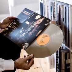 a person holding a record in front of a book shelf filled with books and cds