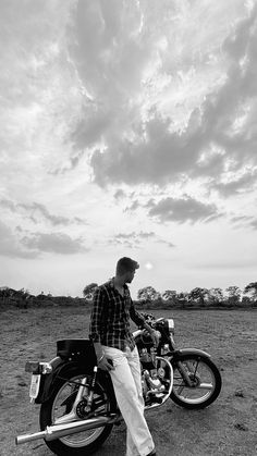 a man is sitting on his motorcycle in the middle of an open field under a cloudy sky