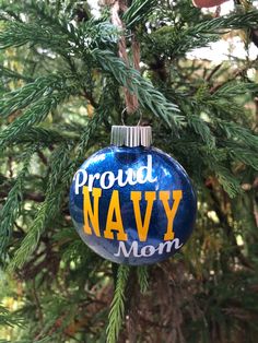 a blue ornament hanging from a tree with the word proud navy mom on it