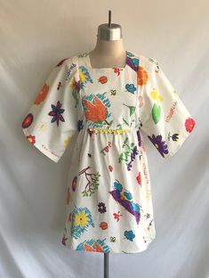 "One-of-a-kind, handmade novelty cotton mini dress made from a 1970's Butterick pattern! Dress features kimono sleeves, square neck, A line silhouette in a vintage Hawaiian print with kids drawings and writing. A hand crocheted piece of yellow cotton lace decorates the front waist seam. Waistline is between an empire and a natural waist. Dress is lined in the bodice and zips up the back with a plastic teeth zipper.  Never worn, made specially for Kinfauns!  Fabric designed and printed in Hawaii Vintage Cotton Mini Dress, Multicolor Cotton Mini Dress For Daywear, White Retro Square Neck Dress, Retro White Square Neck Dress, Vintage Cotton Mini Dress With Square Neck, White Cotton Retro Mini Dress, Playful Cotton Mini Dress For Spring, White Retro Cotton Mini Dress, Retro Multicolor Square Neck Dress