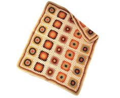 a crocheted blanket with an orange and brown design on the bottom, sitting on a white surface