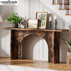 a wooden table with pictures and plants on it next to a stair case in a living room