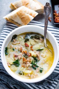 a bowl of soup with spinach, sausage and bread next to it on a towel