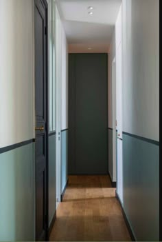 an empty hallway with wooden floors and gray doors on both sides, leading to another room