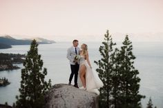 a bride and groom stand on top of a mountain overlooking the water at sunset or dawn