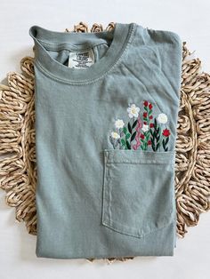 a t - shirt with flowers in the pocket on a wicker place mat next to a woven basket