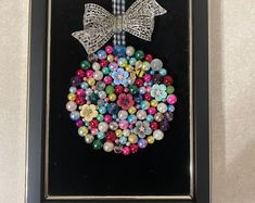 a framed picture with beads in the shape of a christmas ornament and a bow