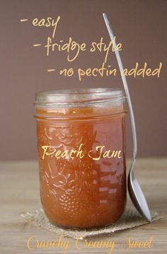 a jar filled with peach jam sitting on top of a table next to a spoon