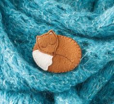 a close up of a knitted surface with a felt fox brooch on it