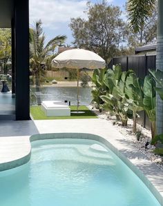 an outdoor swimming pool surrounded by greenery and palm trees, with umbrella over it