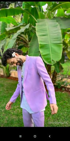 a man in a purple suit and flower in his hair is walking through the grass