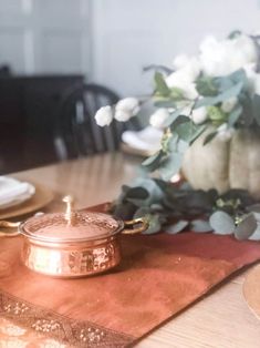 a copper pot sitting on top of a wooden table next to a vase with white flowers