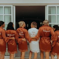 the bridesmaids are wearing orange robes with white writing on them and standing in front of an open door