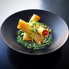 a black plate topped with pasta and spinach