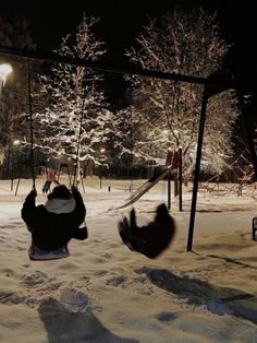 two people on swings in the snow at night