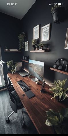 a desk with a computer on it in front of a window and potted plants