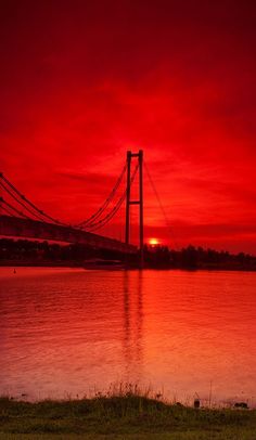 the sun is setting behind a bridge over water