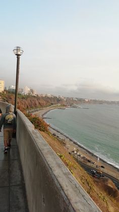 two people are walking up the side of a hill next to the beach and ocean