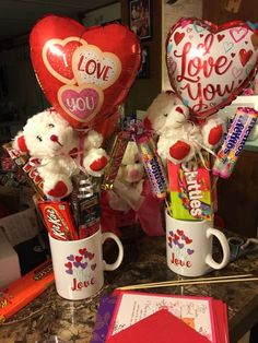 two mugs filled with valentine's day candy and heart shaped balloons on a counter