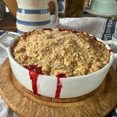 a pie with crumbled topping sitting on top of a wooden platter next to a pitcher