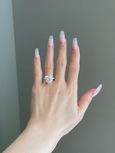 a woman's hand with white and pink manicured nails holding a diamond ring