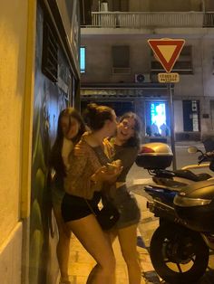 two women standing next to each other in front of a motorbike on the street