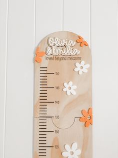 a wooden thermometer with flowers on it sitting on a wall next to a ruler