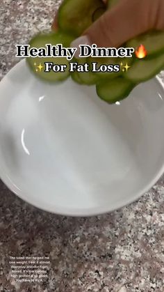 a white bowl filled with meat and veggies next to a fork on top of a table