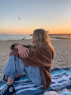 a woman sitting on top of a blanket at the beach