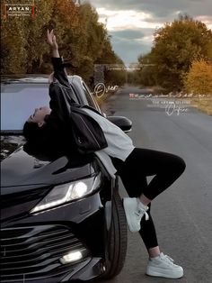 a woman leaning on the hood of a car with her hand up in the air