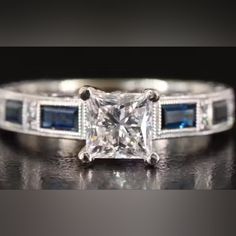 an engagement ring with a princess cut diamond and blue sapphire stones on the sides, set in white gold